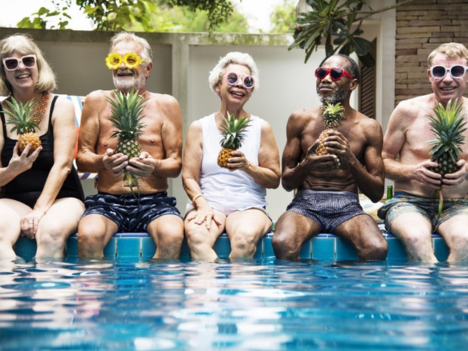 A group of people are in sunglasses sitting on a pool holding pineapples.