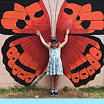 Image of a little girl standing in front of the side of a building with a large butterfly painted on it.