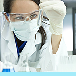 Image of a sceintist analyzing test tubes under a microscope.