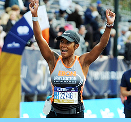 An image of a woman crossing the finish loine at the Boston Marathon with an NBTS Gray Nation shirt on.