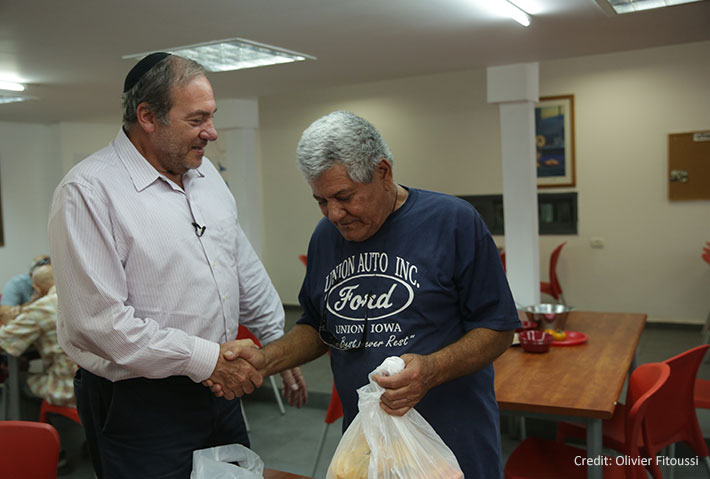 RYE Yechiel Eckstein handing food bag to elderly man