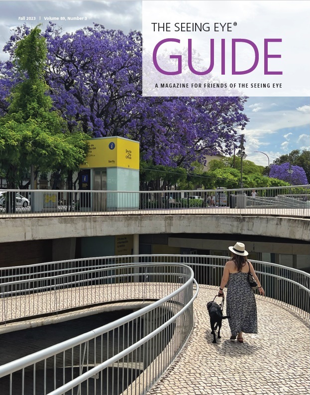The cover of The Guide Fall 2023 shows a Seeing Eye graduate being guided by a black Labrador retriever down a spiral pedestrian ramp.